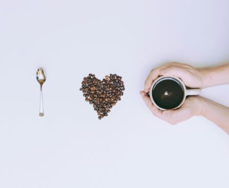 Coffee beans arranged in a heart shape with a mug and spoon on a white background.